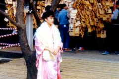 Japan - Tokyo - Ueno Park - In Japan one becomes formally an adult at 18 years of age, but not properly so before the 18 year old goes through this day and its ceremonies. This young woman in her finest clothes has come to the temple to let her picture be taken by her family and perhaps hang a prayer on a wooden board, like the ones in the background. The wishes varies from good exam results, a good job to a good and safe family life, in short everything necessary to make a happy life.